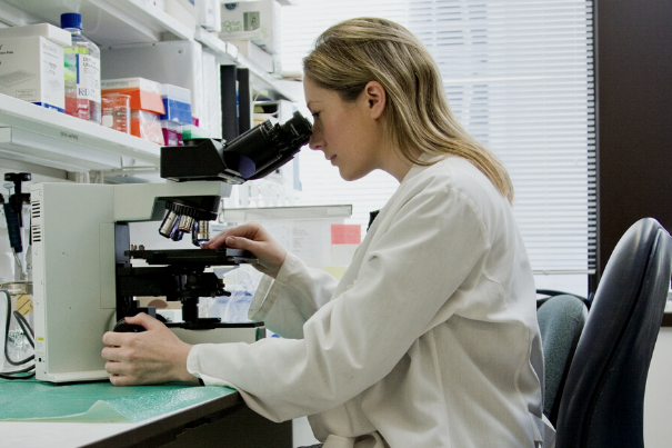 a_woman_in_a_lab_coat_uses_a_microscope
