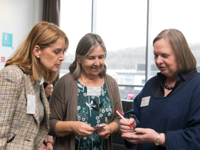 three women talking and making notes