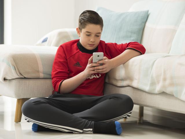 Young boy stat on the floor looking at his phone