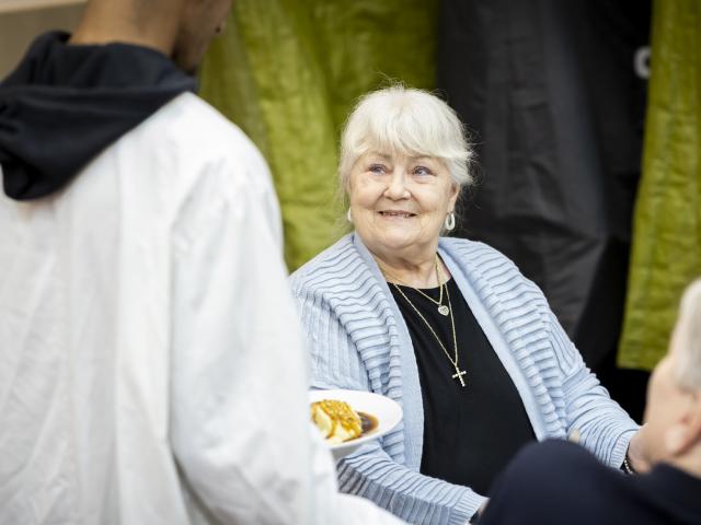 A male assistant handling a plate of food to an older lady.