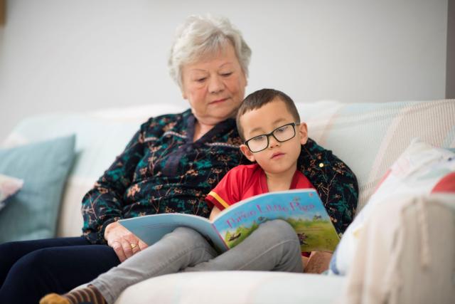 hen wraig yn darllen gyda bachgen ar soffa