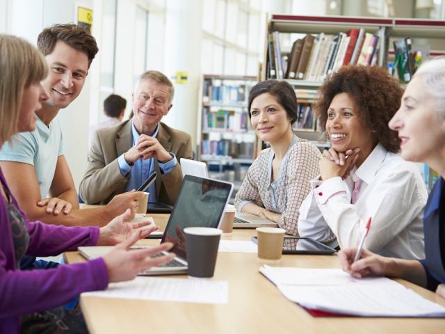 Six people of mixed ethnicities sitting around a table in a library