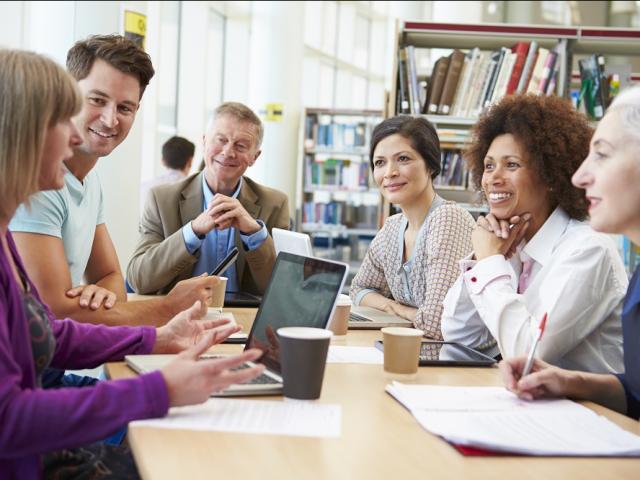 Six people of mixed ethnicities sitting around a table in a library