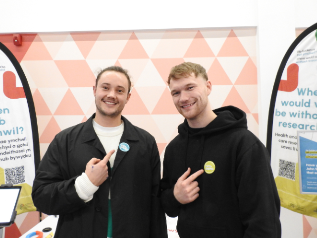 Two young men posing with where would you be without research badge. 