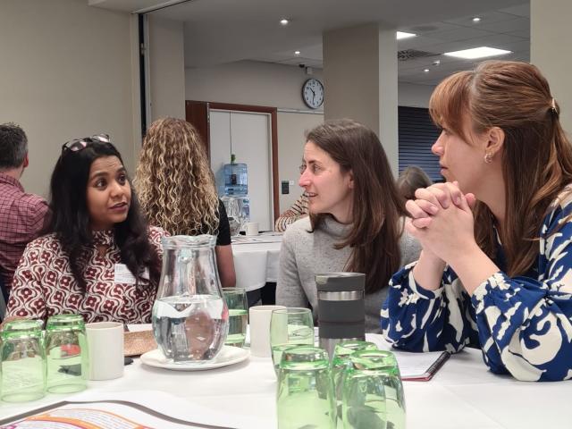 Three women discussing research at a table