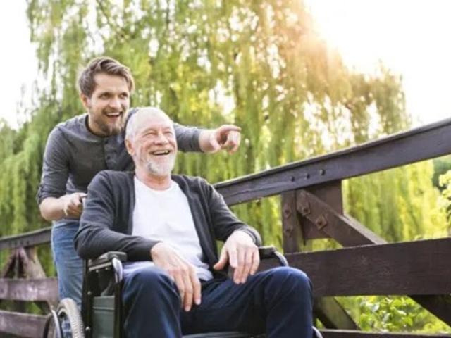 Old man in wheelchair with carer helping them