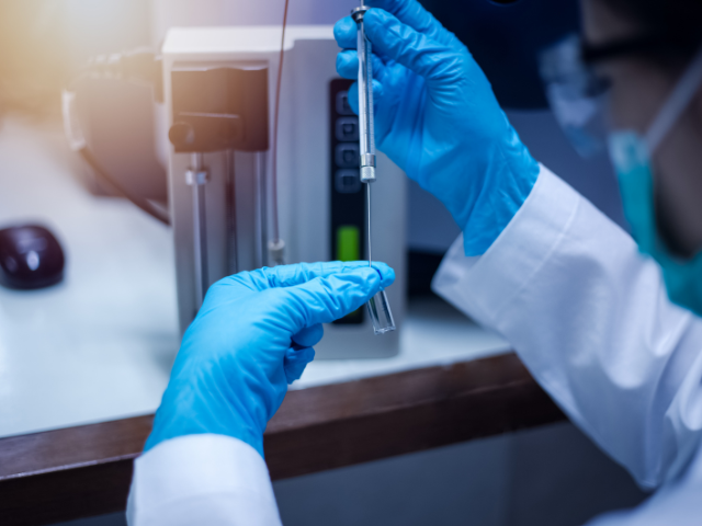Two blue gloved hands holding a test tube in a laboratory type setting