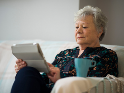 Older person woman using ipad sat on couch