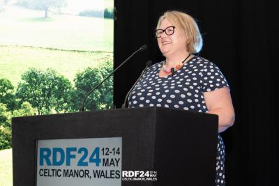 Woman stood on stage at lectern smiling