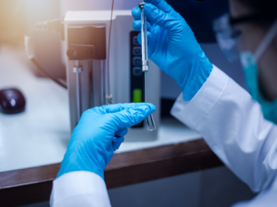 Two blue gloved hands holding a test tube in a laboratory type setting